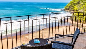 Un balcone con vista sull'oceano e sulla spiaggia, arredato con mobili in vimini e un libro.