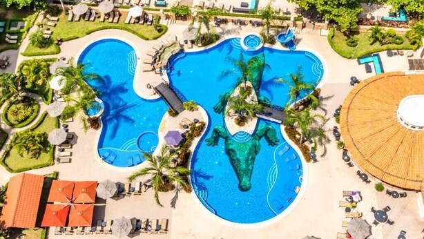 Vista aerea di un resort con diverse piscine, lettini e palme.