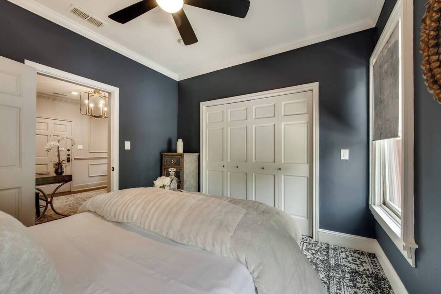 A bedroom with a large bed, a wardrobe, a ceiling fan, and a window.