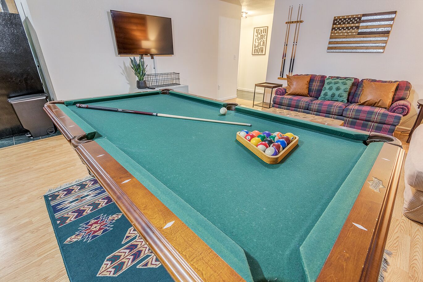 A pool table with balls, a sofa, and a television in a room.
