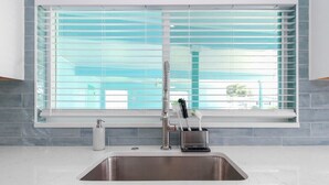 Une cuisine moderne avec un évier en acier inoxydable, une fenêtre avec des stores bleus et un porte-brosses à dents contenant deux brosses à dents.