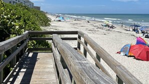 Une promenade en bois menant à une plage où se trouvent des tentes et des parasols.
