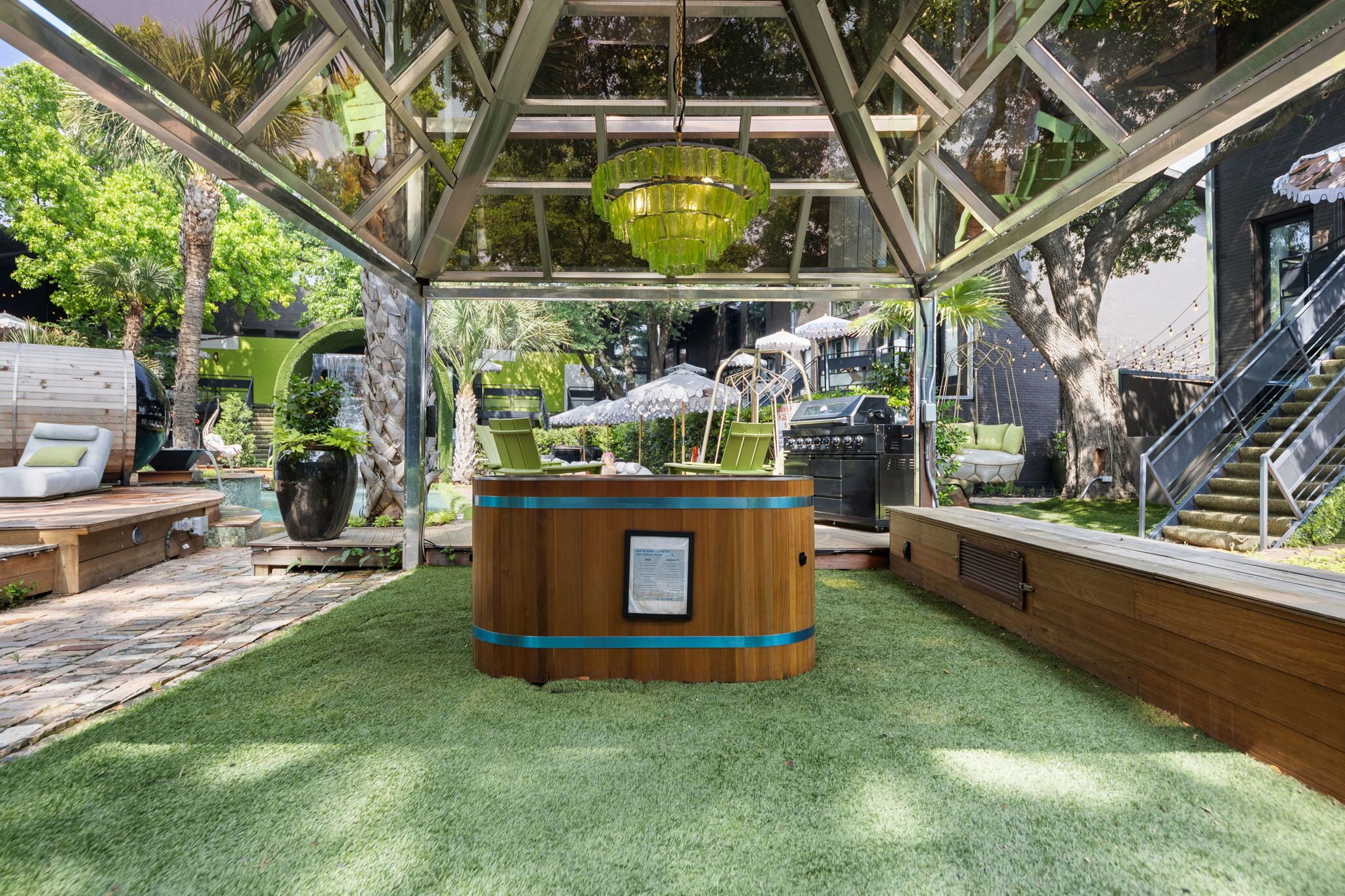 A wooden structure with a central table, surrounded by greenery and a glass ceiling.