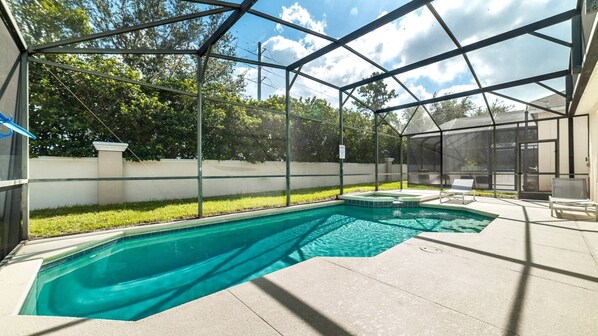 A covered outdoor swimming pool with a hot tub, surrounded by a metal fence and a lawn.
