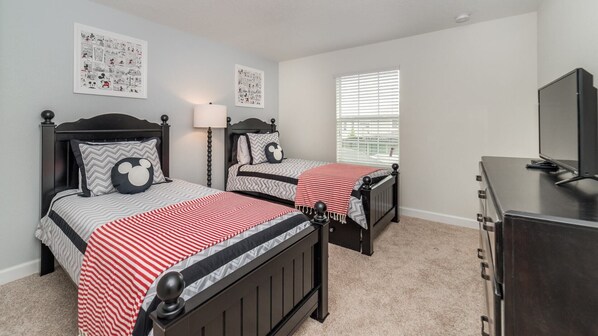 A bedroom with two beds, each with Mickey Mouse themed pillows, a dresser, and a television.