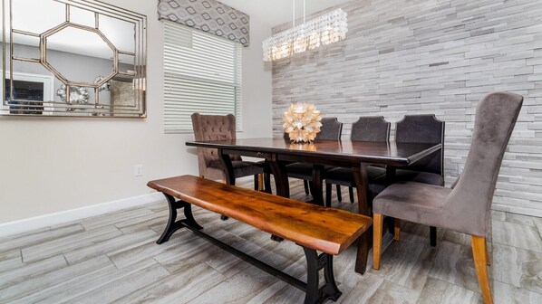A dining area with a wooden table, six chairs, a bench, a chandelier, and a wall-mounted mirror.