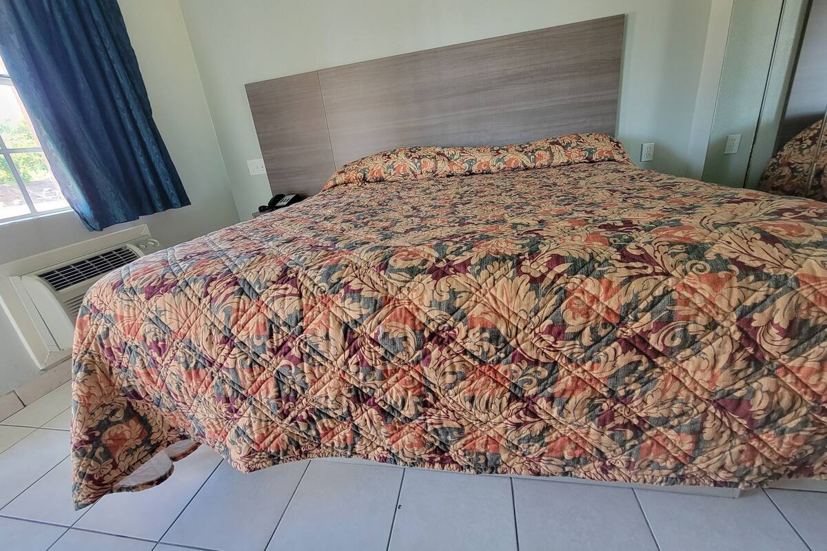 Een slaapkamer met een groot bed, een hoofdbord, een raam met gordijnen en een airconditioner.
