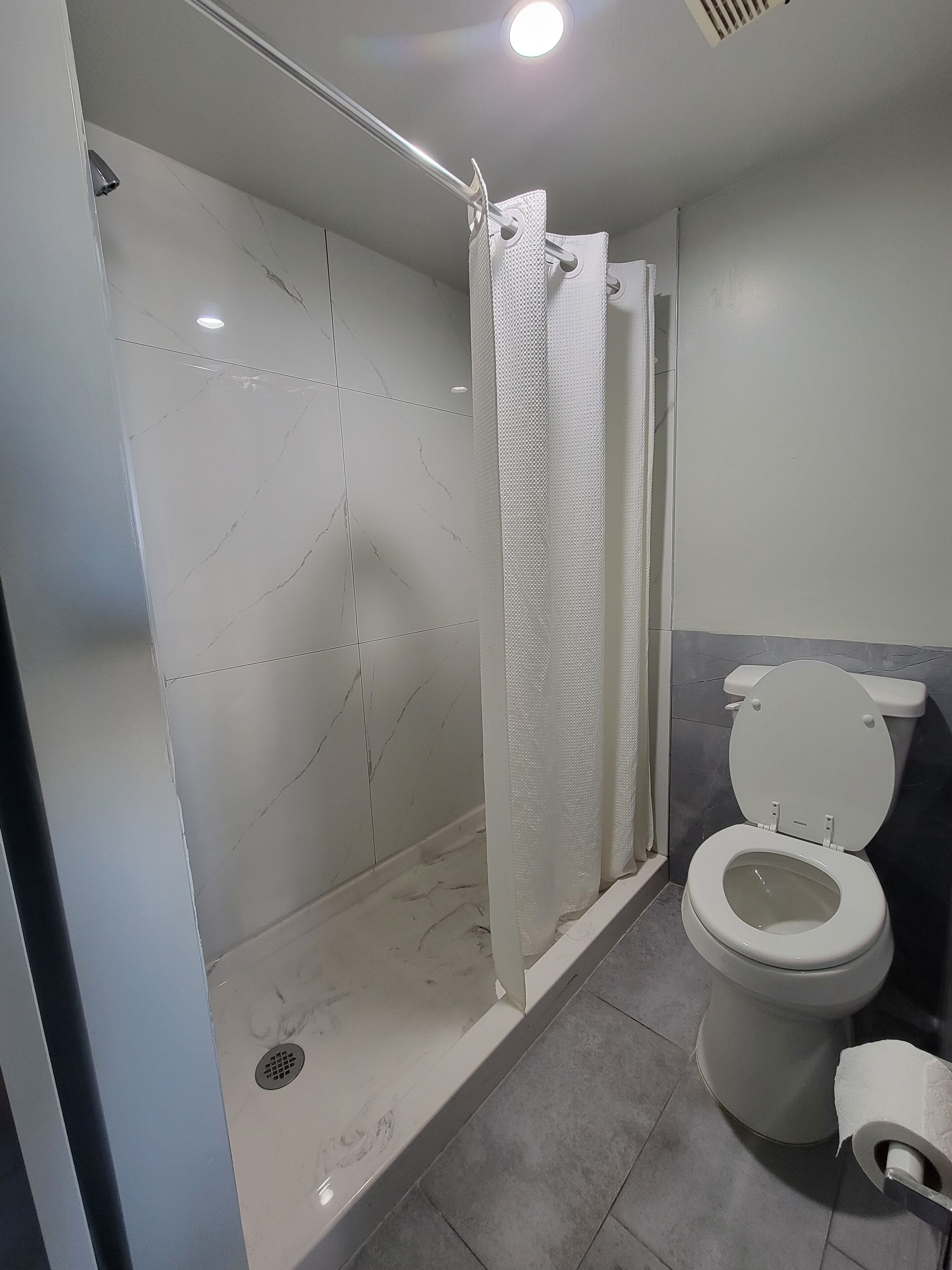 Baño con ducha, inodoro y un rollo de papel higiénico blanco.