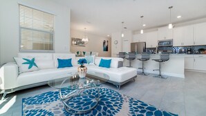 Ein modernes Wohnzimmer mit einem weißen Sofa, einem Glastisch und einem blauen Teppich mit Muster.