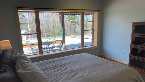 A bedroom with a large bed, a window with a view of outdoor furniture, and a wooden cabinet.