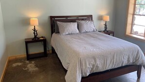 A bedroom with a large bed, two bedside tables with lamps, a window with a view, and a wooden floor.