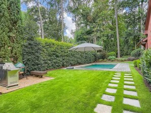 Un patio trasero bien cuidado con piscina, zona de barbacoa y un sendero de piedra.