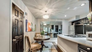 A modern kitchen with dark cabinetry, a round dining table, and a chandelier. - Spacious 1-bed executive condo on Dallas’ historic Swiss Avenue. Enjoy the porch access, high-speed Wi-Fi, king bed with Egyptian-cotton linens, and modern design with upscale finishes—perfect for morning coffee, remote work, or relaxing evening (Dallas)