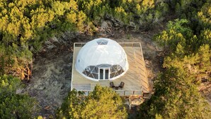 Vue aérienne d’une structure en forme de dôme, dotée d’une terrasse en bois et d’un espace aménagé pour s’asseoir.