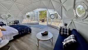 Une tente spacieuse équipée d’un lit, d’un canapé, d’une petite table et offrant une vue sur l’extérieur.