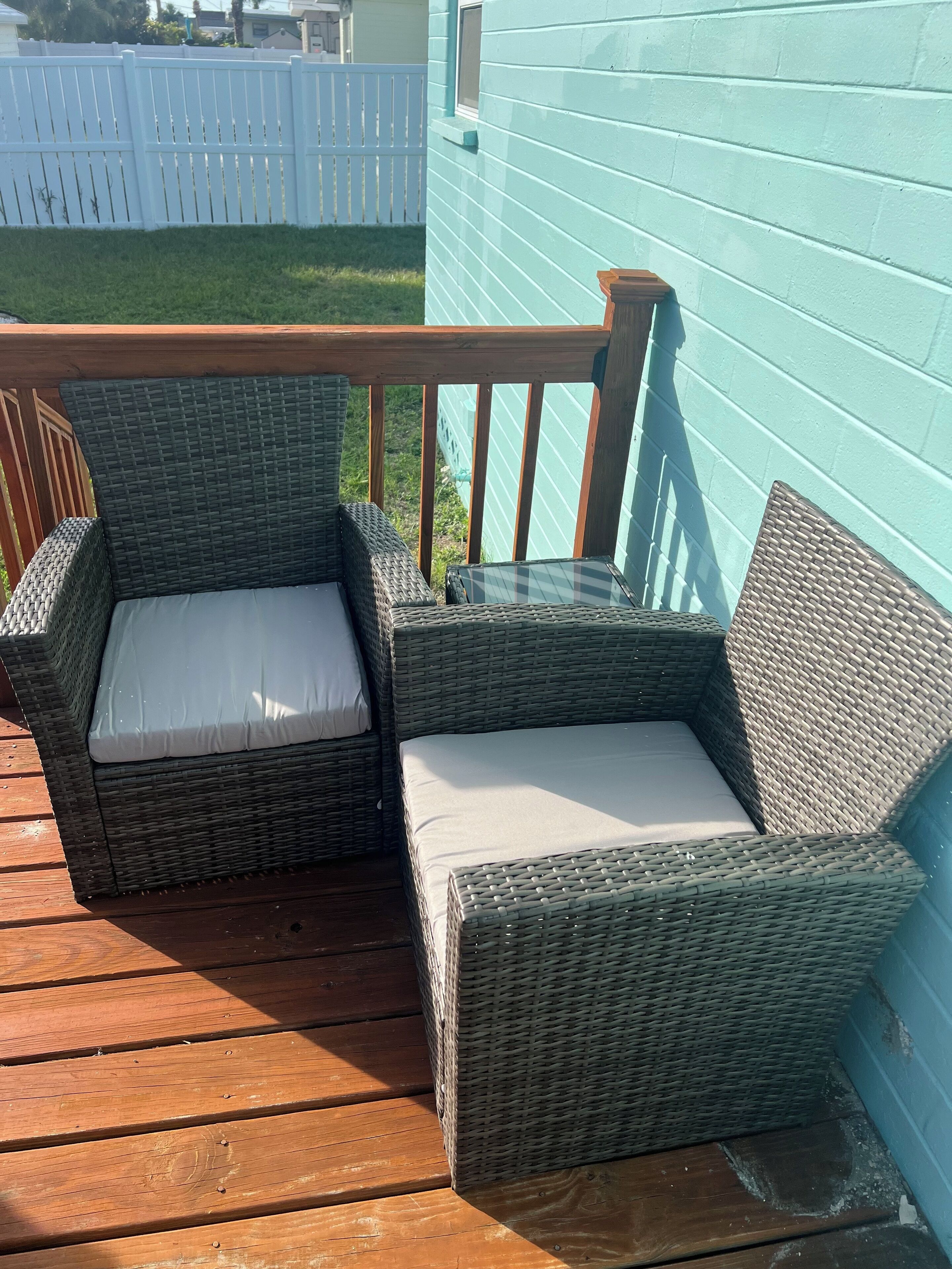 Two wicker chairs with cushions on a wooden deck.