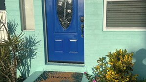 A house with a blue door, a welcome mat, and a small garden with yellow flowers. - Beautiful 2/1 Home - Walking Distance to the Beach (Port Orange)