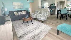 A living room with a sofa, armchair, coffee table, and a dining area with chairs and a table. - Beautiful 2/1 Home - Walking Distance to the Beach (Port Orange)