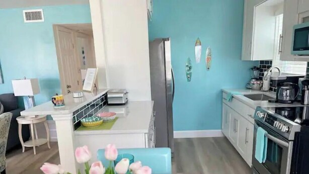 A modern kitchen with a teal wall, a dining area with a table and chairs, and a living room with a sofa and a lamp. - Beautiful 2/1 Home - Walking Distance to the Beach (Port Orange)