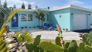 A two-story house with a blue exterior, a garage, and a small front yard with chairs and plants. - Beautiful 2/1 Home - Walking Distance to the Beach (Port Orange)