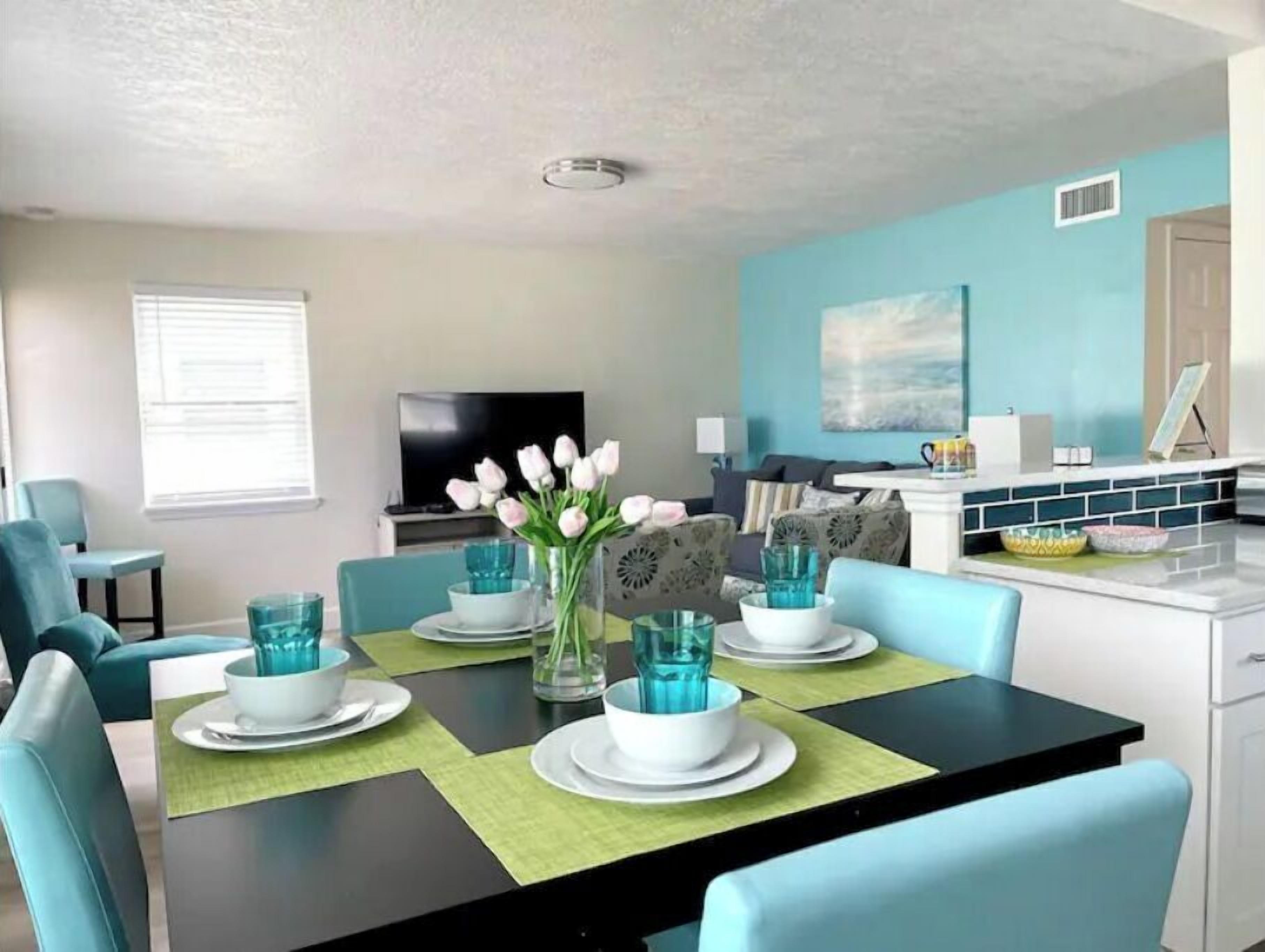 A modern dining area with a black table, teal chairs, and a vase of white flowers.