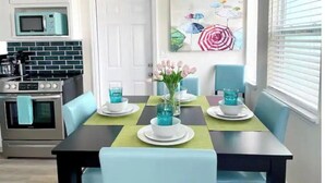 A dining area with a table set for four, a kitchen with modern appliances, and a beach-themed painting on the wall. - Beautiful 2/1 Home - Walking Distance to the Beach (Port Orange)