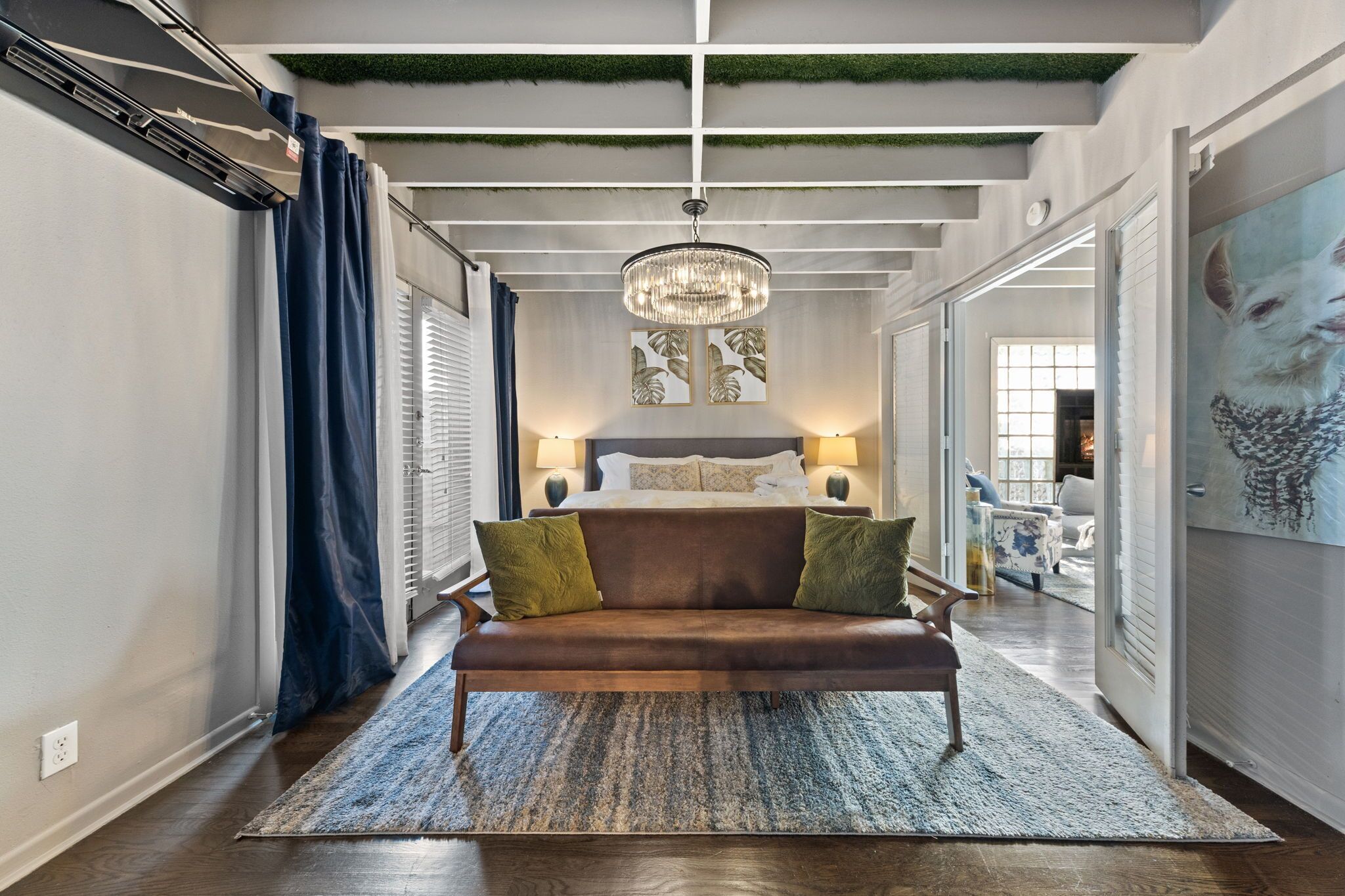 A hallway with a brown leather sofa, a chandelier, and a large painting of a dog.