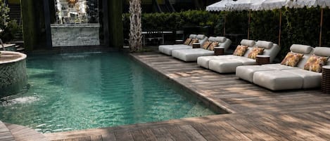 A pool area with a waterfall feature, wooden deck, and outdoor seating.