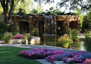 Stroll through a tranquil garden oasis with a central water feature, surrounded by lush greenery and vibrant flowers.