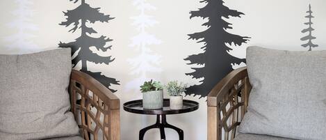 A cozy seating area with two cushioned chairs and a small round table, featuring a wall with a forest-themed mural.
