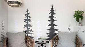 Ein Zimmer mit zwei Holzstühlen mit grauen Kissen, einem runden weißen Tisch und einem schwarzen Teppich.