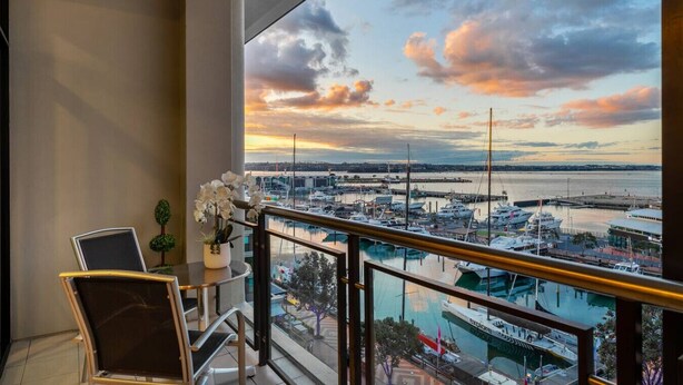 Un balcon donnant sur une marina et des bateaux, une table avec des chaises et un pot de fleurs.