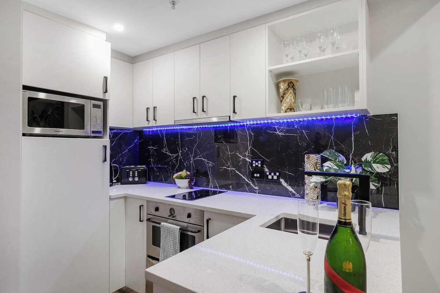 A modern kitchen with white cabinets, a black marble backsplash, a built-in microwave, and a wine bottle on the counter.
