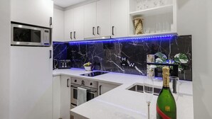 Une cuisine moderne avec des armoires blanches, un pare-feu en marbre noir, un four à micro-ondes encastré et une bouteille de vin posée sur le comptoir.