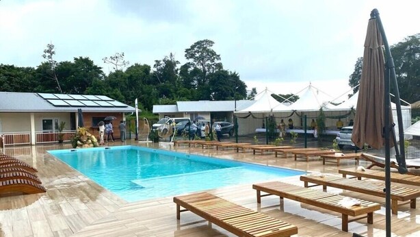 A swimming pool with wooden loungers and a covered area with umbrellas. - Hôtel Belle Terre Resort (Macouria)