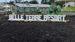 A sign for Belle Terre Resort with a tropical sculpture and flags in the background. - Hôtel Belle Terre Resort (Macouria)