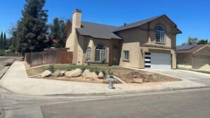 A two-story house with a stone facade, a garage, and a landscaped front yard with rocks and a fire hydrant. - Newley remodeled and furnished home! (fresno)