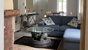 A living room with a blue sofa, a glass coffee table, and a brick fireplace. - Country house next to a golf course, in the Fontainebleau region. (Voulx)
