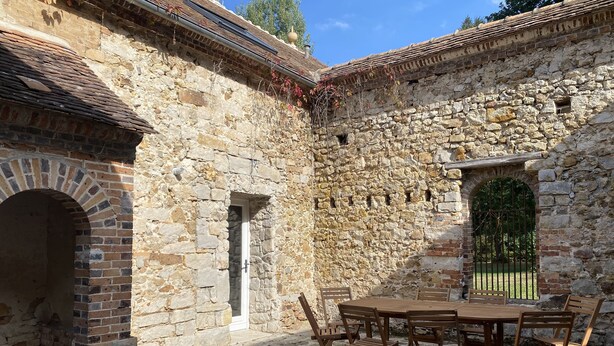 A stone building with a brick archway and a wooden table with chairs in the courtyard. - Country house next to a golf course, in the Fontainebleau region. (Voulx)