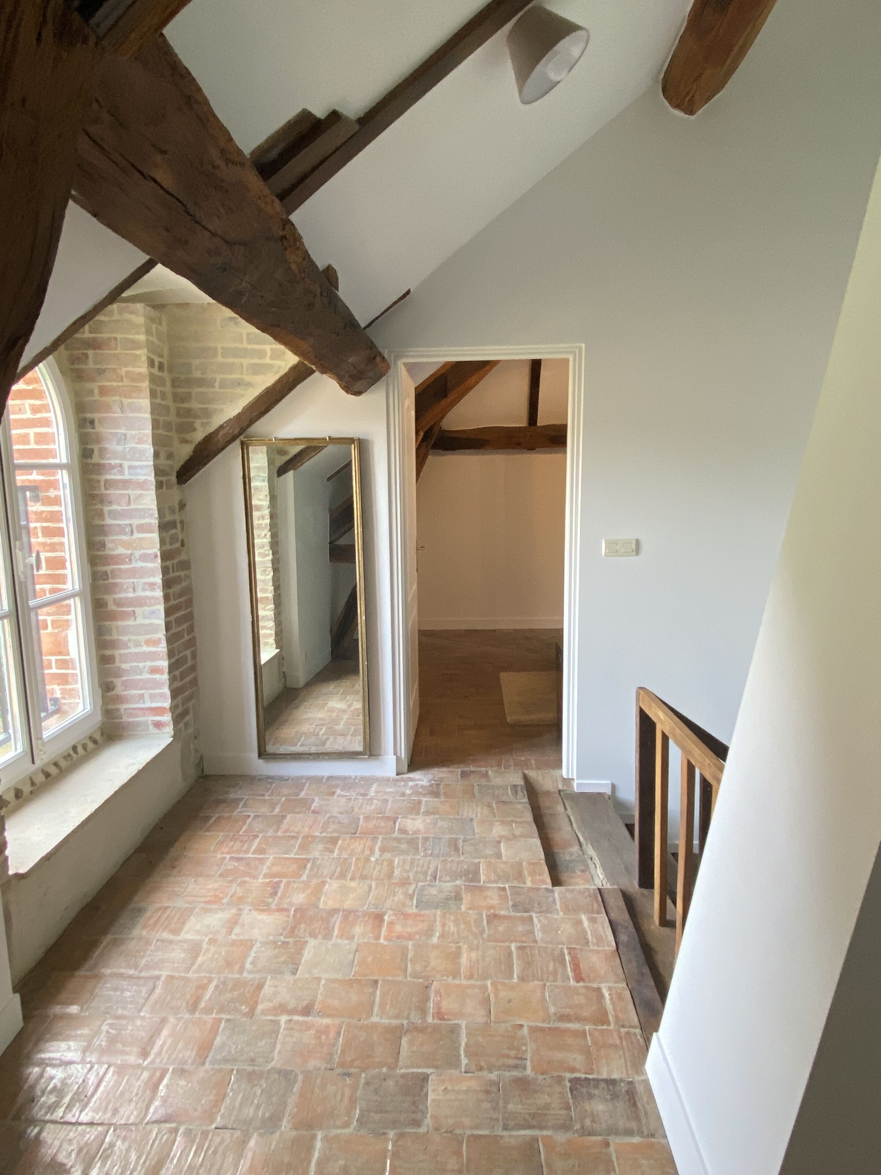 Una habitación con vigas de madera a la vista, pared de ladrillo y un espejo grande.