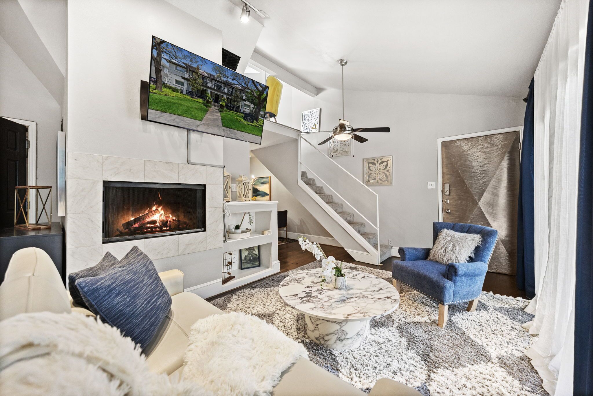 Een moderne woonkamer met een open haard, een ronde salontafel, een blauwe fauteuil en een trap.