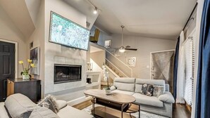 En moderne stue med pejs, sofaarrangement, sofabord og tv ophængt på væggen.