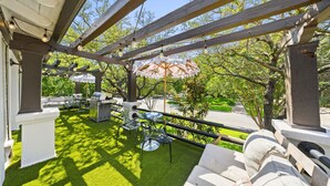 En udendørs patio med pergola, kunstgræs, udendørs møbler og grill.