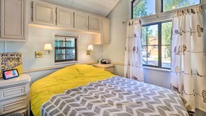 A bedroom with a bed, a nightstand, a lamp, a window with curtains, and a sign on the wall.