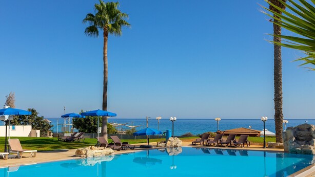A clear blue sky, a swimming pool with lounge chairs and umbrellas, and a view of the sea. - Protaras Pallini Seaside Suite (Protaras)