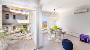 A modern apartment with a balcony, a dining area with white chairs and a table, and a large window offering a view. - Protaras Pallini Seaside Suite (Protaras)