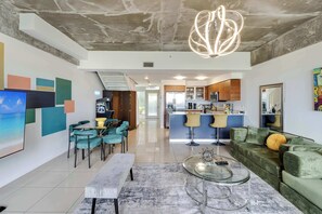 Un salon moderne avec une table basse en verre, un canapé et un coin repas avec des chaises de couleur turquoise.