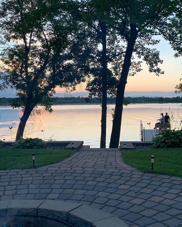 A paved pathway leading to a lakeside area with trees and a view of the water.