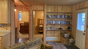 A cozy cabin interior with a wooden interior, a sofa, a bookshelf, and a door leading to another room.