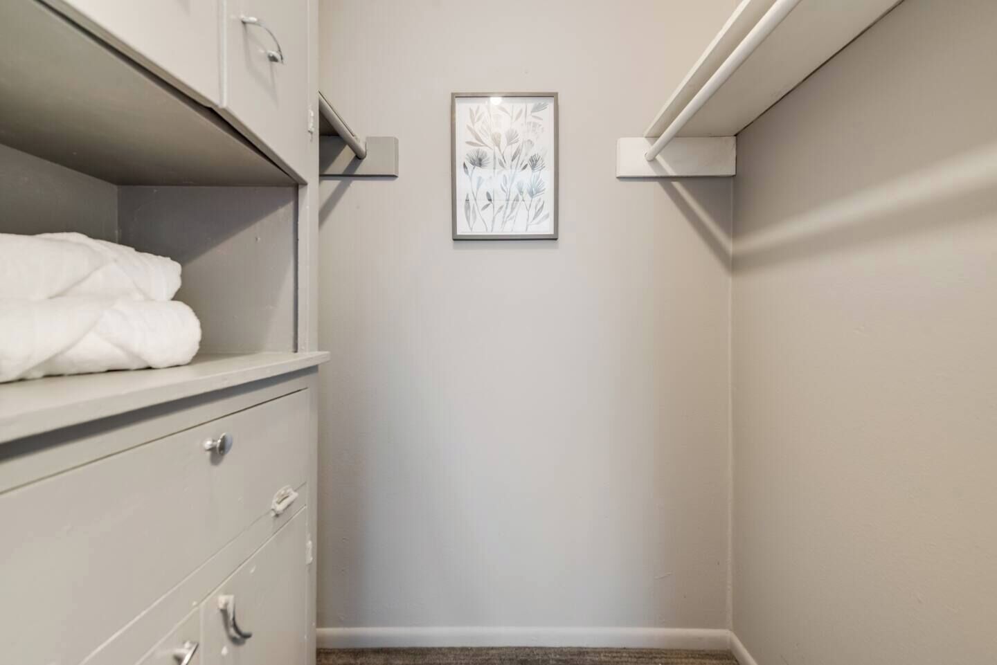 A walk-in closet with a white dresser, a framed floral artwork on the wall, and a towel on the top shelf.